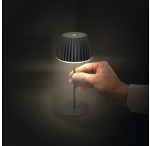 Liten batteridriven bordslampa med plisserad skärm, hållen i en hand