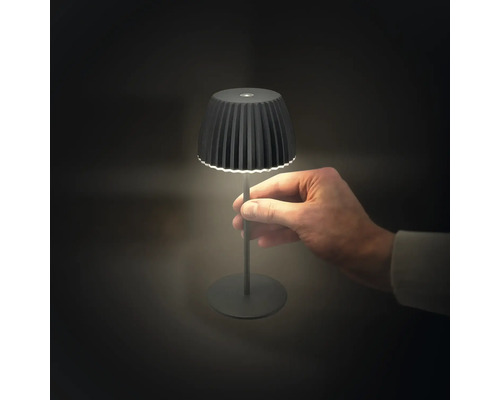 Liten batteridriven bordslampa med plisserad skärm, hållen i en hand