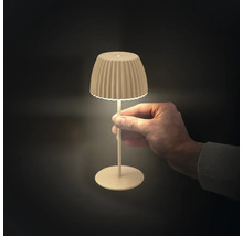 En hand håller i en liten, modern LED-bordslampa med en räfflad lampskärm och smal fot som avger ett varmt ljus.