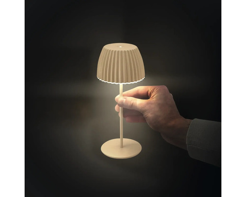 En hand håller i en liten, modern LED-bordslampa med en räfflad lampskärm och smal fot som avger ett varmt ljus.