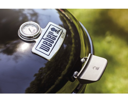 Detaljvy av en klotgrill med Weber-logotyp, temperaturindikator och lockhandtag