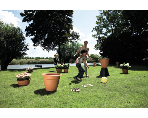 Trädgårdsscen med lekande barn, blommor i krukor och en grön gräsmatta