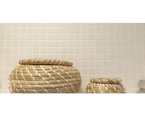 Två flätade korgar med lock framför en vägg med små fyrkantiga plattor.