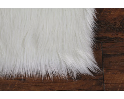 Detaljvy av en vit lurvig matta på ett trägolv