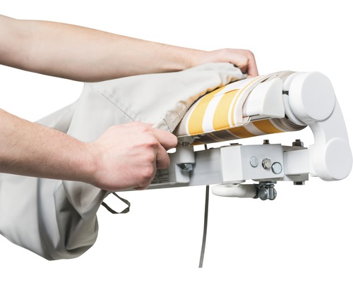 Person drar ett skyddande hölje över en markis med ett randigt mönster.