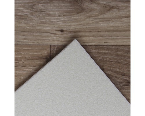 Detaljvy av en vit vinylplatta på ett trägolv.