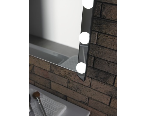 Detalj av en upplyst spegel bredvid en tegelvägg i badrummet