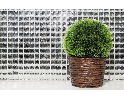 Dekorativ grön konstgjord växt i brun kruka framför en mosaikvägg