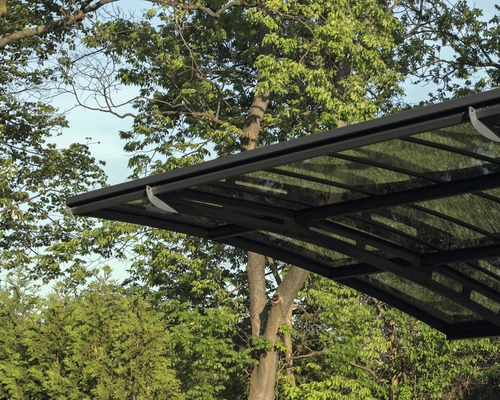 Detaljvy av carport med stålram och transparent tak framför träd