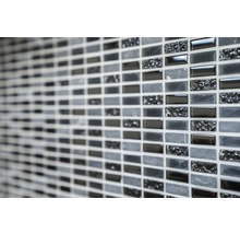Detaljbild av en vägg med mosaikplattor i olika gråtoner och texturer.