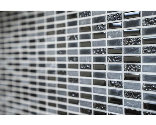 Detaljbild av en vägg med mosaikplattor i olika gråtoner och texturer.