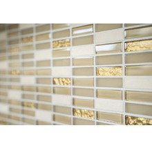 Närbild av en vägg med mosaikplattor i beige, guld och gräddfärgade toner