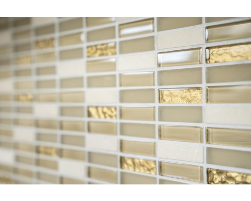 Närbild av en vägg med mosaikplattor i beige, guld och gräddfärgade toner