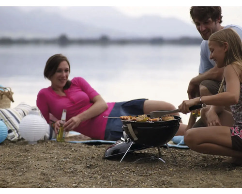 Familj grillar vid sjön med en kolgrill, medan mamman kopplar av med en drink