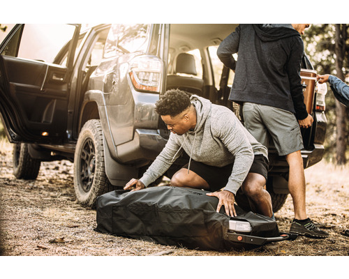 Person packar en väska framför ett fordon.