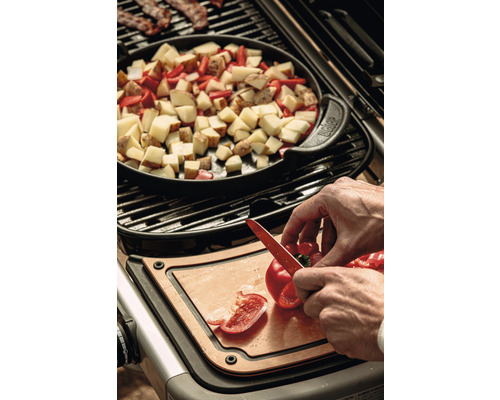 Matlagning på en grill med potatis, paprika och bacon, med en person som skär paprika på en skärbräda.