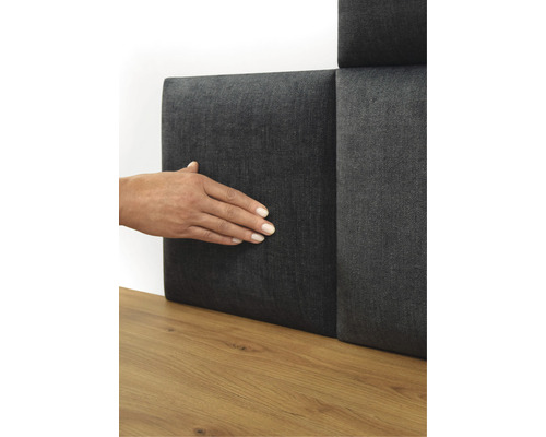 Person berör en grå väggpanel med textilbeläggning på ett trägolv.