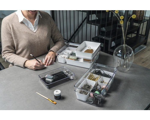 Scen med en person som sitter vid ett skrivbord med transparenta förvaringslådor fyllda med diverse kontorsmaterial.