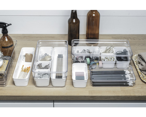 Flera transparenta lådorganiserare med diverse kontorsmaterial på en arbetsyta.