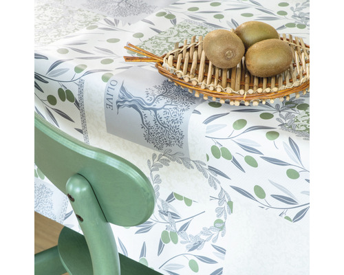 Bordsduk med olivmönster och kiwifrukter i en korg på ett bord