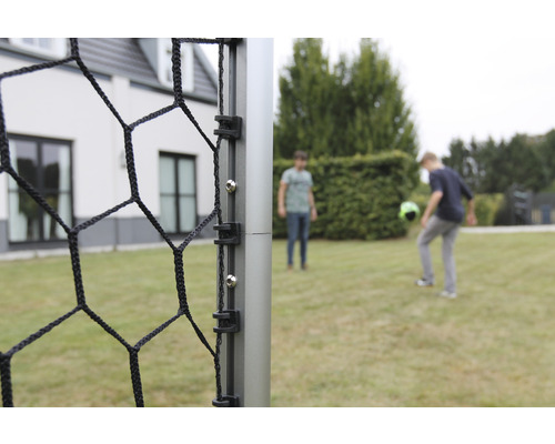 Detaljvy av en fotbollsmål med nät och två personer som spelar i bakgrunden