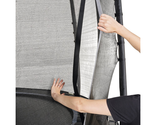 Närbild av ett trampolinskyddsnät som delvis öppnas av två händer för att frigöra ingången