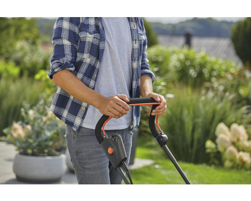 En person använder en gräsklippare i trädgården.