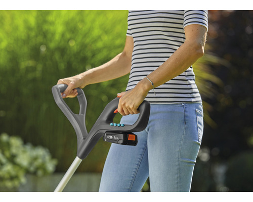 Kvinna använder en batteridriven grästrimmer i trädgården.