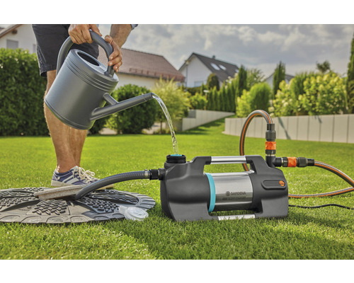 Person fyller trädgårdspump med vattenkanna i trädgården