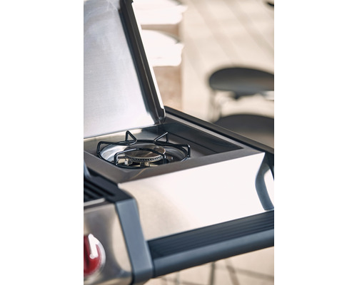 Detaljbild av en gasolgrill i rostfritt stål med öppet lock och synlig brännare