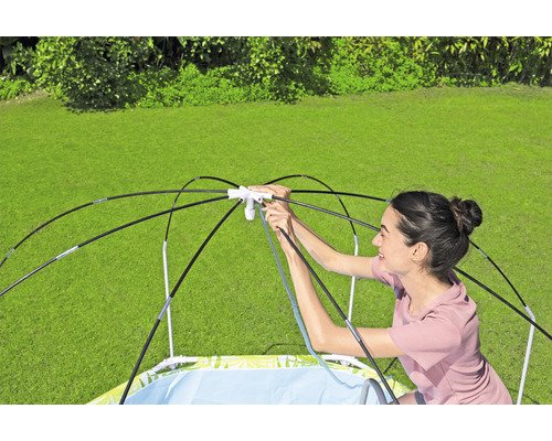 En kvinna sätter upp en barnpool med solskydd i trädgården.