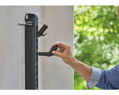 Väggmonterad trädgårdsredskapshållare med person som fäster en slanganslutning