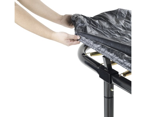 Person fäster ett skyddshölje på en trädgårdstrampolin.