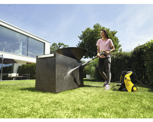 Kvinna rengör utomhusskulptur med högtryckstvätt i trädgården.