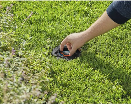 En person justerar en infälld grässprinkler i gräsmattan.