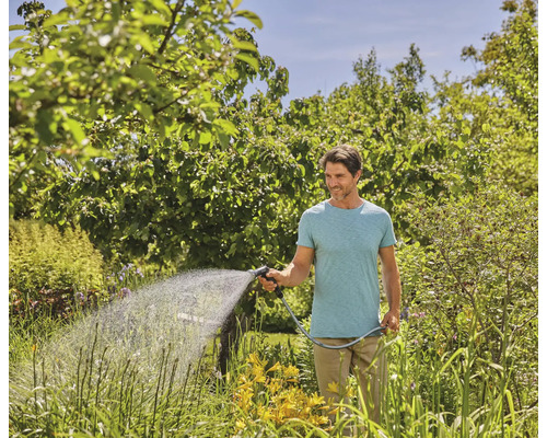 Man vattnar trädgård med trädgårdsslang och sprutmunstycke