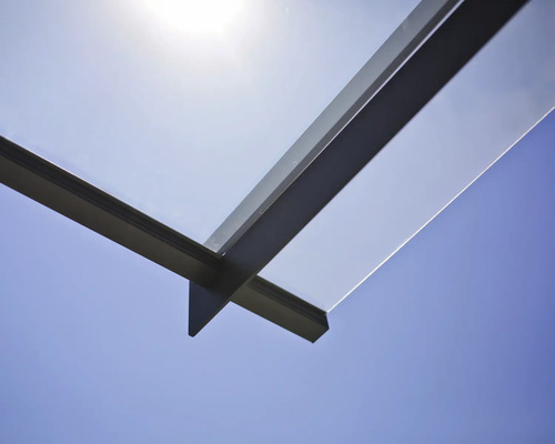 Detaljvy av ett terrasstak av glas och metall mot en blå himmel