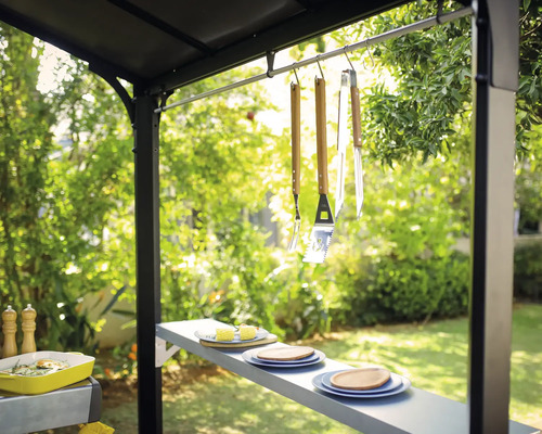 Utomhusgrillscen med grillverktyg, porslin och tillbehör under en trädgårdspaviljong.