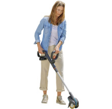 Kvinna använder en batteridriven fogrengörare i trädgården.