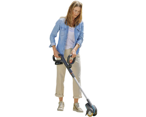 Kvinna använder en batteridriven fogrengörare i trädgården.