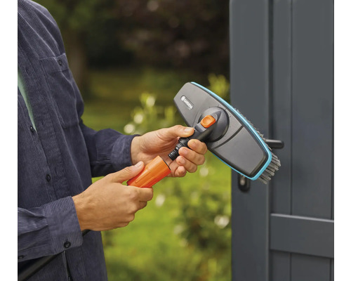 En person ansluter en borste till en trädgårdsslang för rengöringsarbete utomhus.