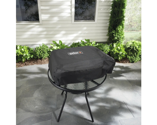 Weber-logotyp på ett svart grillskydd på ett runt bord utomhus