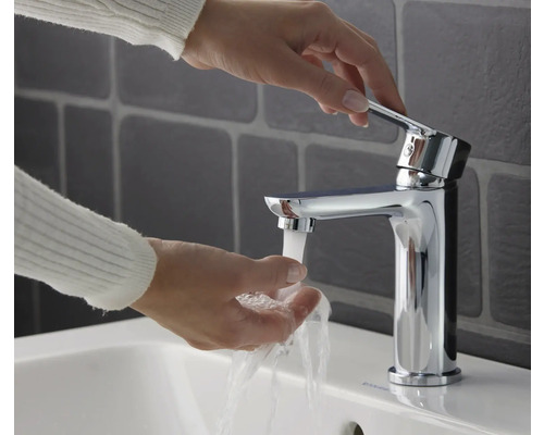 Kvinna tvättar händerna under en kromad tvättställsblandare.