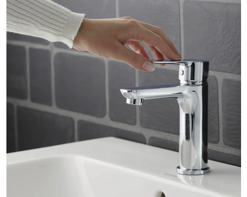 En hand manövrerar en förkromad tvättställsblandare på ett tvättställ.