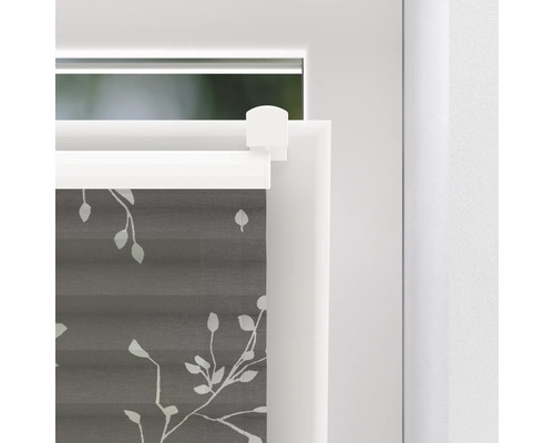 Närbild av en grå plisségardin med bladmönster på ett fönster