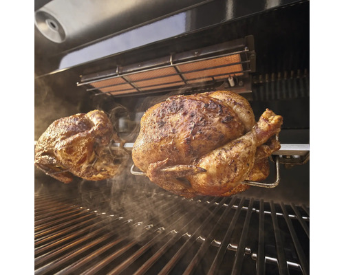 Två kycklingar på ett roterande spett i en grill.