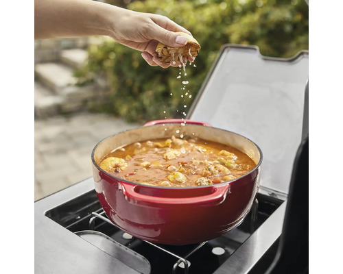 En person pressar citron över en röd gryta på en grill.