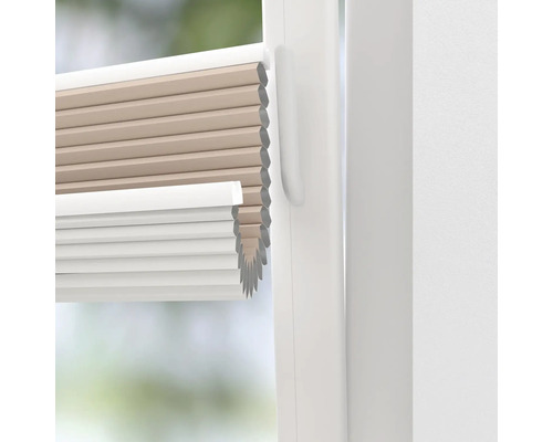 Närbild av en beige och vit plisségardin i ett fönster