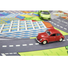 Lekmatta med gatumönster med en röd och en grön leksaksbil på den