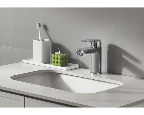 Badrumshandfat med armatur, tandborstmugg och dekorativt ljus.